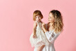 © LIGHTFIELD STUDIOS - Mother in white dress holding girl in white dress on pink background.