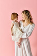 © LIGHTFIELD STUDIOS - Curly-haired mother and cute girl in white dress stand before a vibrant pink background.