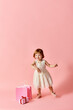 © LIGHTFIELD STUDIOS - Little girl in white dress with pink gift bags against pink backdrop.