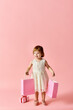 © LIGHTFIELD STUDIOS - A little girl in a white dress joyfully holds pink shopping bags on a pink background.