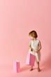 © LIGHTFIELD STUDIOS - Adorable girl in white dress holding shopping bags on pink background.