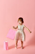 © LIGHTFIELD STUDIOS - Little girl in white dress holding pink shopping bags on a pink background.