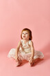 © LIGHTFIELD STUDIOS - Adorable girl in white dress sitting gracefully on pink backdrop.