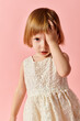 © LIGHTFIELD STUDIOS - Charming little girl in white dress striking a pose against soft pink backdrop.