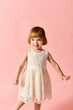 © LIGHTFIELD STUDIOS - Adorable girl in white dress confidently posing on pink background.