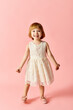 © LIGHTFIELD STUDIOS - Little girl in white dress poses gracefully on pink backdrop.
