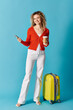 © LIGHTFIELD STUDIOS - A stylish woman holding a cup of coffee and a suitcase on a blue background.