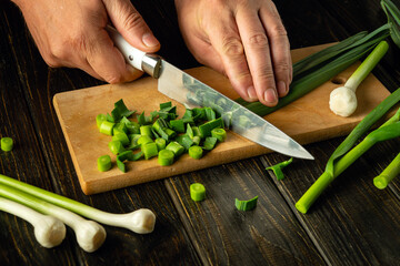 Wall Mural - Cooking a flavorful vegetarian dish with garlic. The chef hands use a knife to cut young garlic on a wooden kitchen board