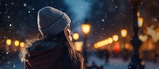 Wall Mural - a girl in fashionable winter attire looks up with her hand at her head against the backdrop of a win