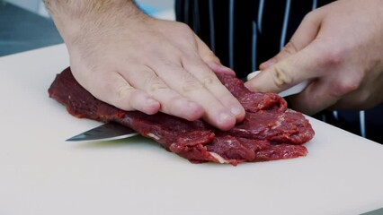 Canvas Print - Chef cutting fresh beef meat into pieces on kitchen table, close up