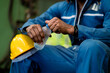 © KANGWANS - A man in a blue jumpsuit is holding a bottle of water. He is wearing a yellow hard hat
