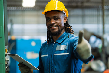 A man in a blue work uniform is holding a tablet and giving a thumbs up. He is wearing a yellow hard hat and a blue shirt