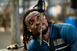 © KANGWANS - A man with dreadlocks is looking at a drill. The man is wearing a blue shirt and a blue jacket
