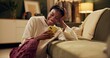 © peopleimages.com - Happy, laugh and black woman with phone on sofa for online chat, communication and networking. Relax, home and person on smartphone for social media, funny website and internet news in living room