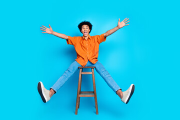 Poster - Full length photo of cheerful positive guy dressed orange shirt sitting stool having fun isolated blue color background