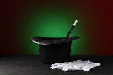 Wall Mural - Magician's hat, wand and gloves on black wooden table against dark background