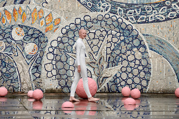 Wall Mural - Young hairless girl ballerina with alopecia in white futuristic suit dancing outdoor among pink spheres on abstract mosaic Soviet background, symbolizes self expression and acceptance of unique beauty