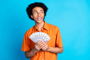 Poster - Photo of cheerful positive guy dressed orange shirt eyewear rising money fan looking empty space isolated blue color background