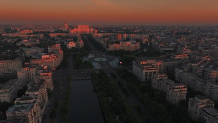 Wall Mural - Bucharest from above. Aerial 4K video with Unirii Square, fountains, library, boulevard and Palace of the Parliament during a beautiful summer orange sky sunrise. Travel to Romania landmarks.
