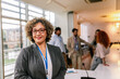 © Mediteraneo - Portrait of older African American businesswoman standing in front of her colleagues.