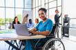 © Barry - Happy, successful young disabled black female in a wheelchair, working in a tech company. in an open plan office with diverse workforce.