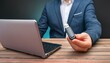 © blackdiamond67 - A man holds a flash drive in his hand against the background of a laptop lying on a wooden table.