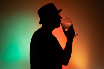 Portrait of an unidentified man in silhouette drinking liquid from a transparent glass.