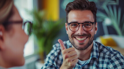 Wall Mural - Young professional wearing eyeglasses gives thumbs-up in a contemporary office environment