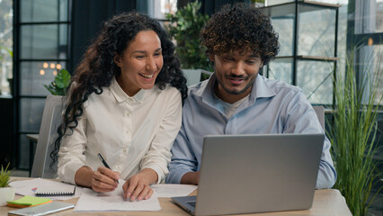 Multiracial business partners happy diverse colleagues Indian businessman and Arabian businesswoman win online project on laptop achievement happy office team workers employees celebrate success deal