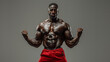 Muscular man flexing arms in studio lighting, wearing red shorts, intense expression, grey background.