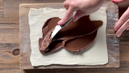 Poster - chef spreads chocolate cream on rolled out sheet of puff pastry for making cookies, top view. Food closeup