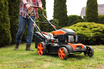 Wall Mural - Man cutting green grass with lawn mower in garden, closeup