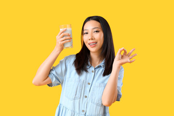 Wall Mural - Young Asian woman with glass of milk showing OK on yellow background