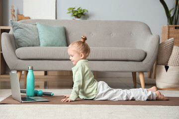 Poster - Cute little girl practicing yoga on mat while watching online tutorial in living room