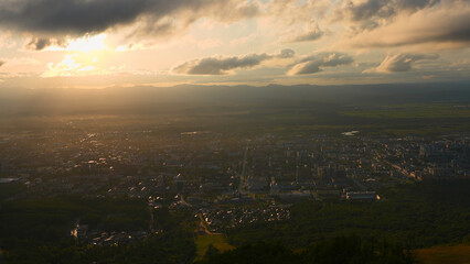 Wall Mural - Top view of city in green valley with sun on horizon. Clip. Beautiful landscape of sunny green valley with town on summer day. Bright sun shines down on valley with town