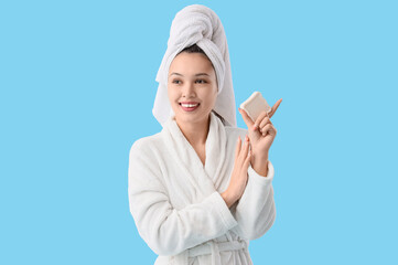 Sticker - Young Asian woman in bathrobe with soap on blue background