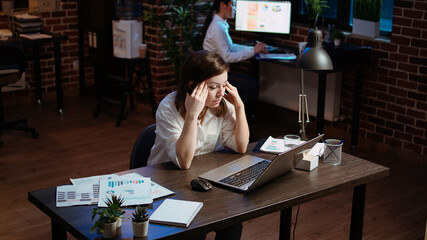 Tired employee struggling to remain focused at workspace desk, feeling overworked and waiting to go home. Bored businesswoman sighing in office while working overnight, camera A