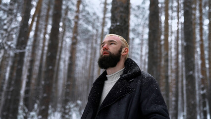 Wall Mural - Man relaxing in the winter forest, the concept of unity with nature. Media. Young blond man thinking about life in snowy wood.