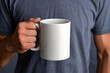 © Moose - A mockup of an all white blank mug being held by the right hand, man wearing blue tshirt