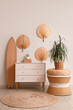 © Pixel-Shot - Surfboard, houseplant and chest of drawers near white wall in room