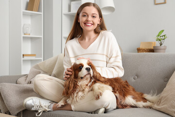 Wall Mural - Young woman with adorable cavalier King Charles spaniel sitting on sofa at home