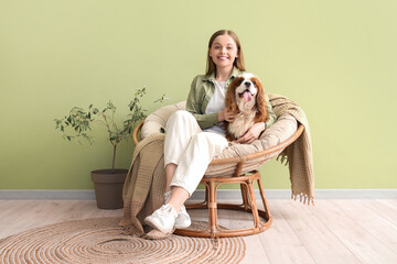 Wall Mural - Young woman and adorable cavalier King Charles spaniel sitting on armchair near green wall at home