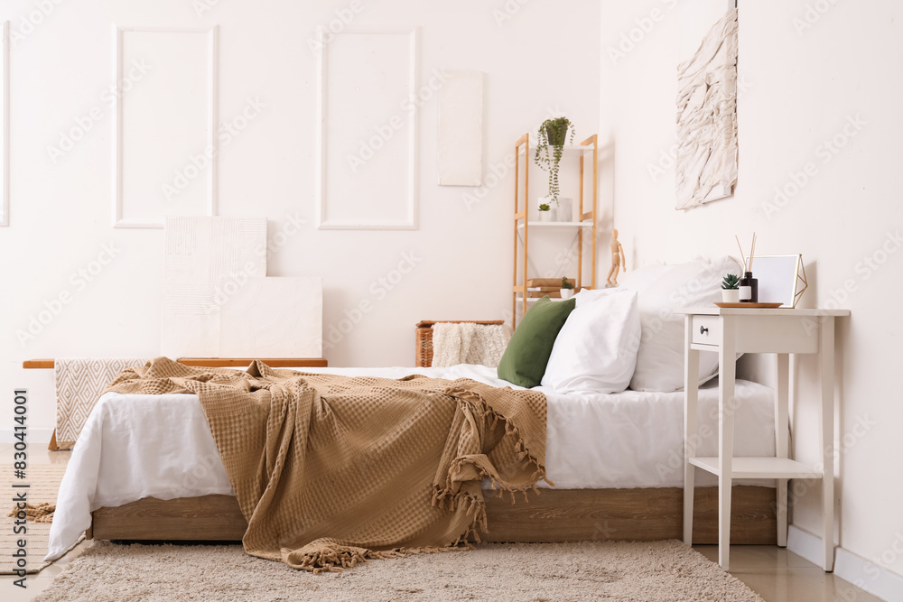 Interior of light bedroom with cozy bed and reed diffuser on bedside table
