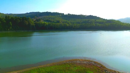 Wall Mural - Peaceful aerial push-in and pan-left shot from Lago di San Ruffino, the lake's finely rippling aquamarine body of water extending from the green shore to greater distances, with water & air creatures