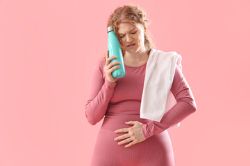 Wall Mural - Female trainer with water bottle suffering from menstrual cramps on pink background