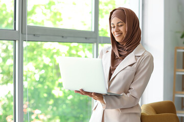 Wall Mural - Muslim businesswoman working with laptop near window at home