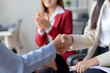 © amnaj - Business professionals shaking hands during a successful meeting, with an encouraging coworker clapping in the background, modern office setting.
