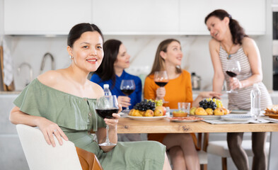 Wall Mural - Asian woman drinking wine in company of friends at home party in kitchen