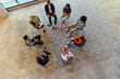 © .shock - Top view of a diverse group of young business entrepreneurs gathered in a circle for a meeting, discussing corporate challenges and innovative solutions within the modern confines of a large