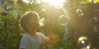 © Waris - child blowing soap bubbles, A child blowing bubbles in the backyard, watching with delight as the bubbles float and shimmer in the sunlight